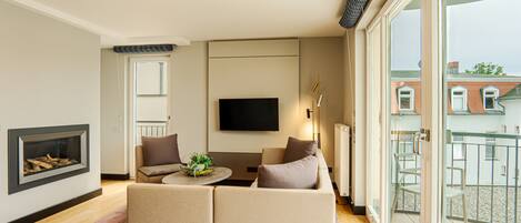 A modern living room with a fireplace, a sofa set, a flat-screen TV, and a balcony with a view of buildings.