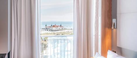 A hotel room with a large window offering a view of a beach and buildings.