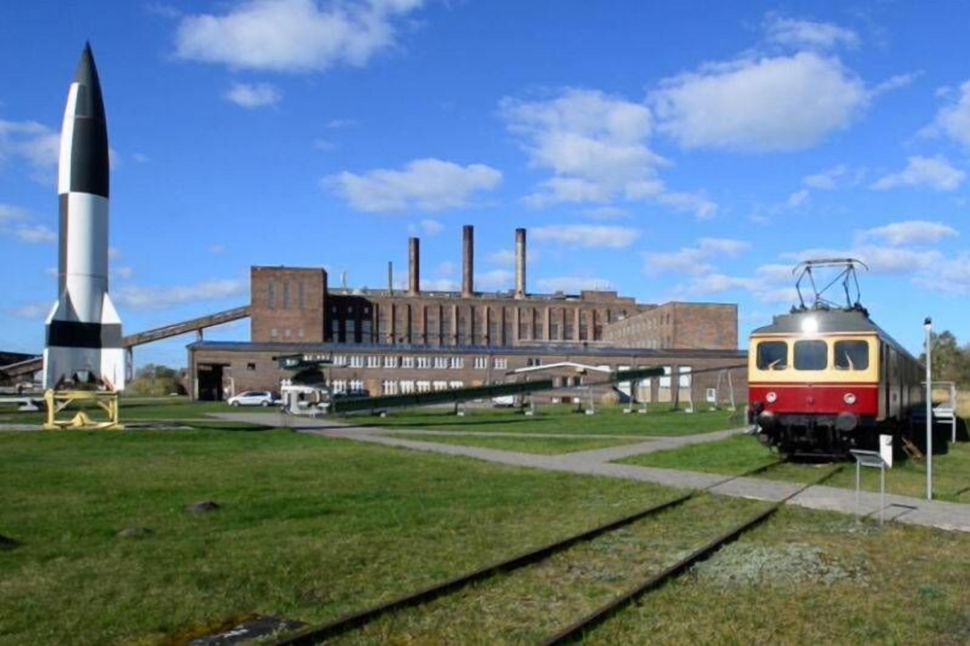 A rocket on display, a train, and a building with multiple chimneys.