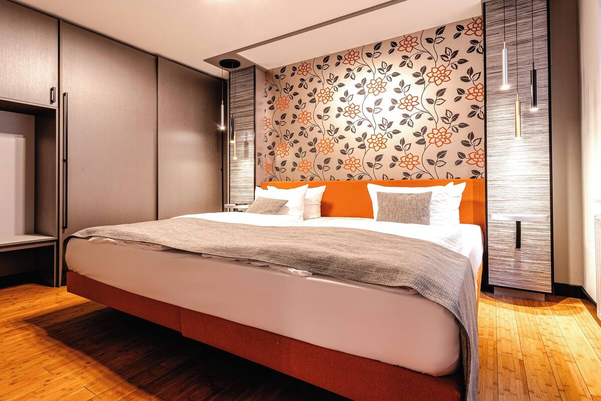 Une chambre moderne avec un grand lit, un plancher en bois et un mur décoratif orné d’un motif floral.