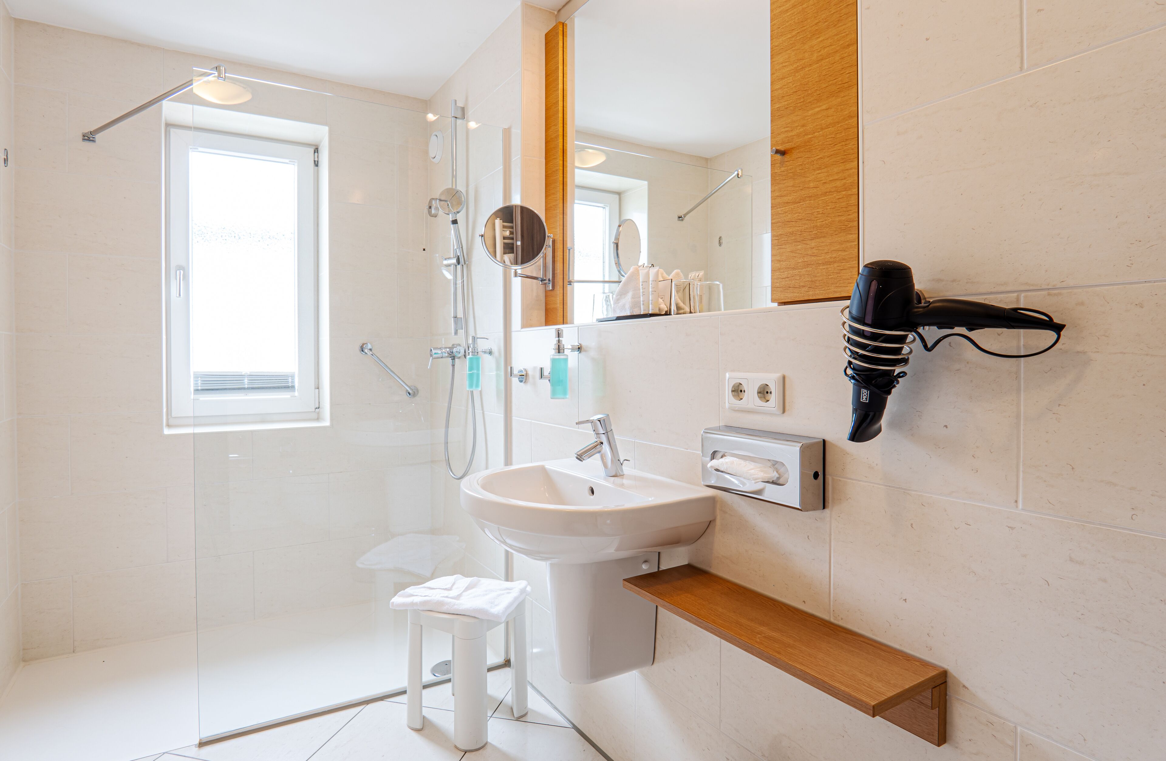A modern bathroom with a glass shower enclosure, a white sink, and a wooden shelf.