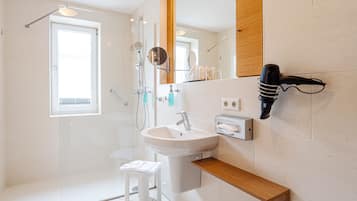A modern bathroom with a glass shower enclosure, a white sink, and a wooden shelf.