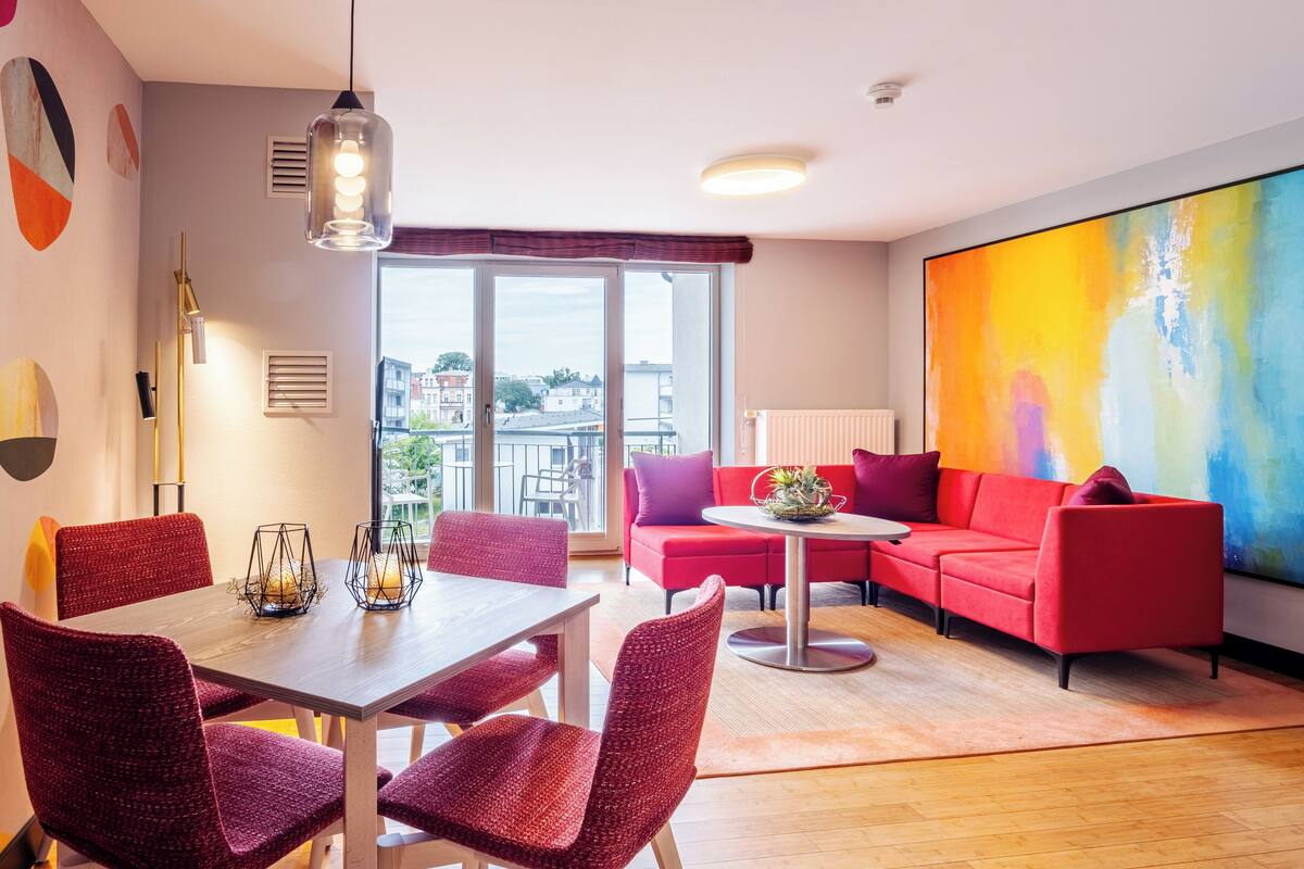 Un salon moderne avec un canapé rouge, une table à manger avec des chaises et un grand tableau abstrait accroché au mur.