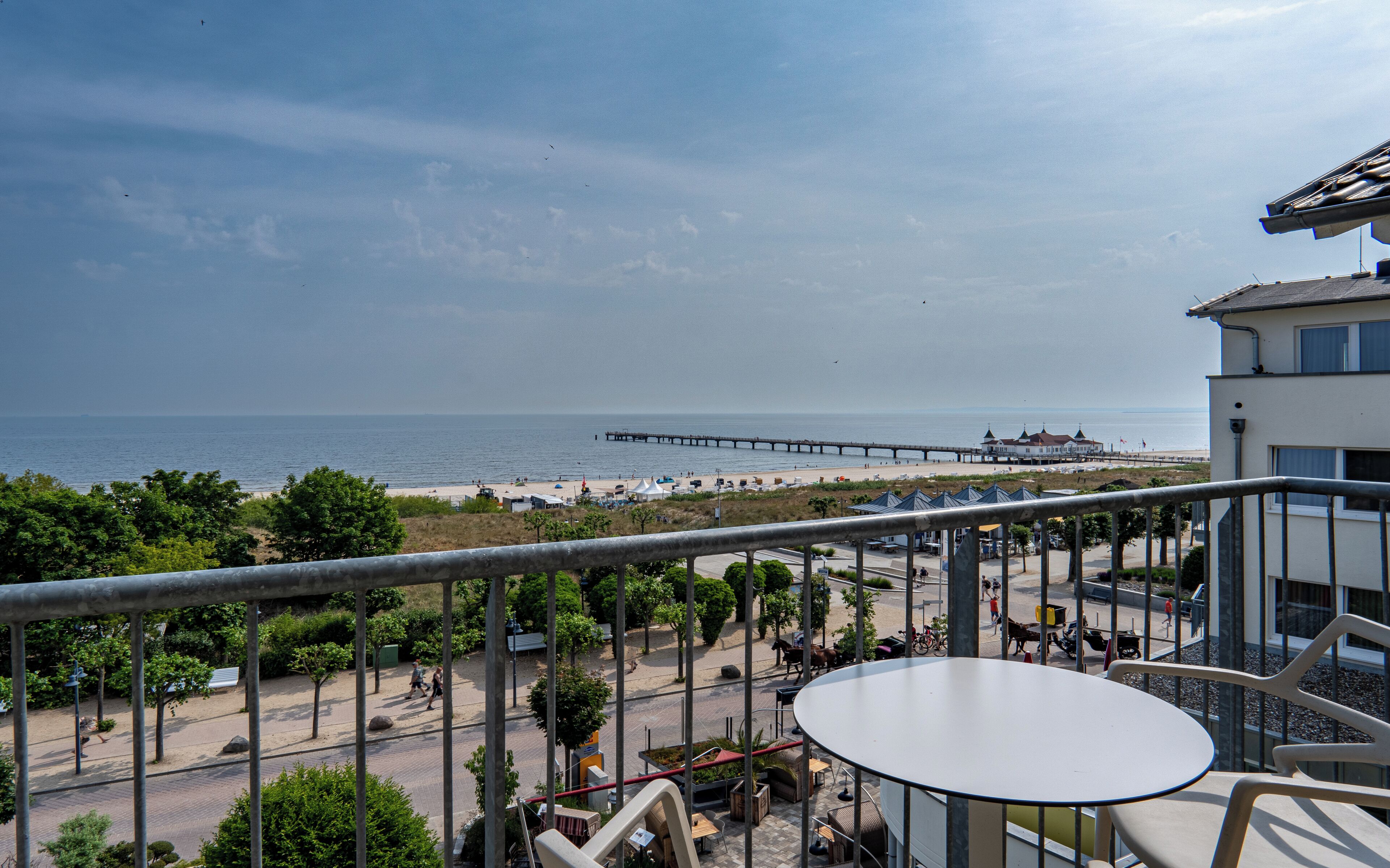 A balcony with a view of the beach, a pier, and a building with a white facade.