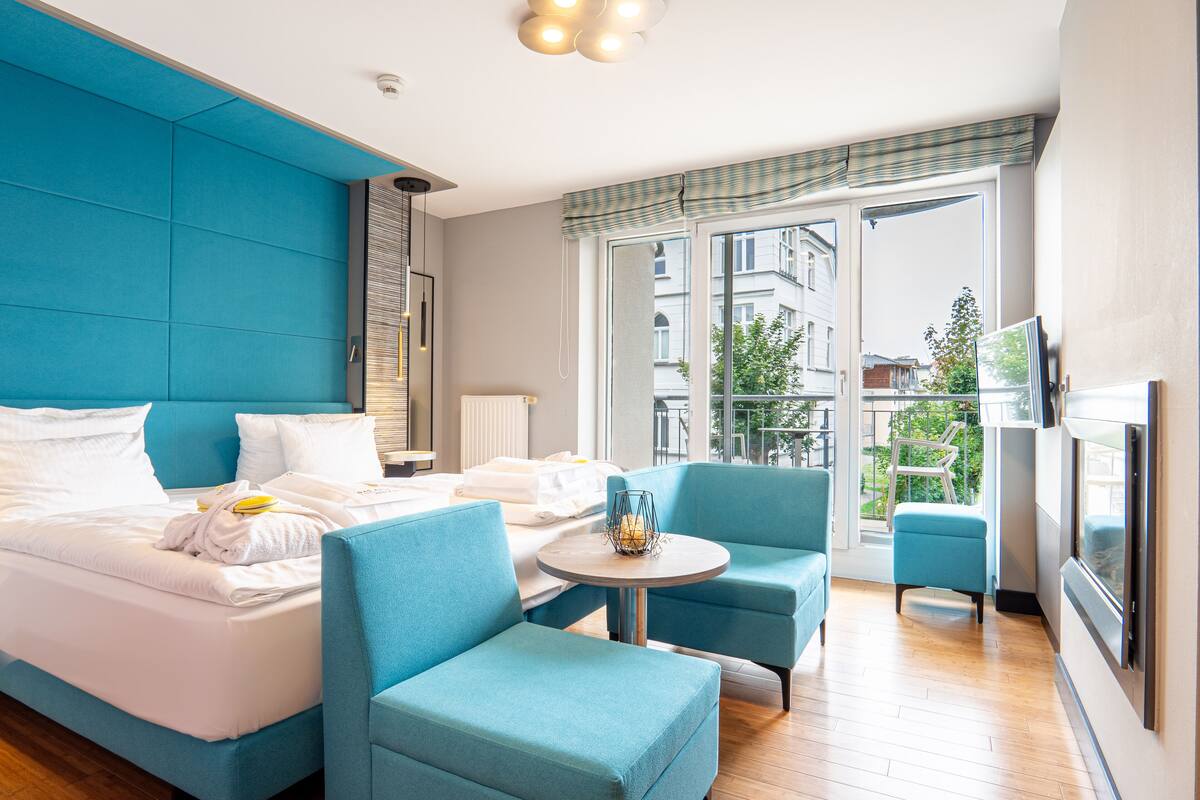 Une chambre d’hôtel avec un grand lit, deux fauteuils bleus, une petite table et un téléviseur.