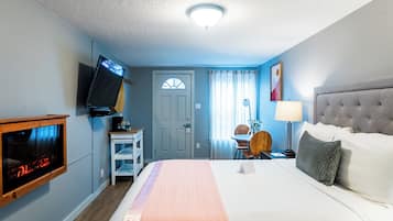 A hotel room with a bed, a television mounted on the wall, a desk with a chair, a lamp, and a door with a window.
