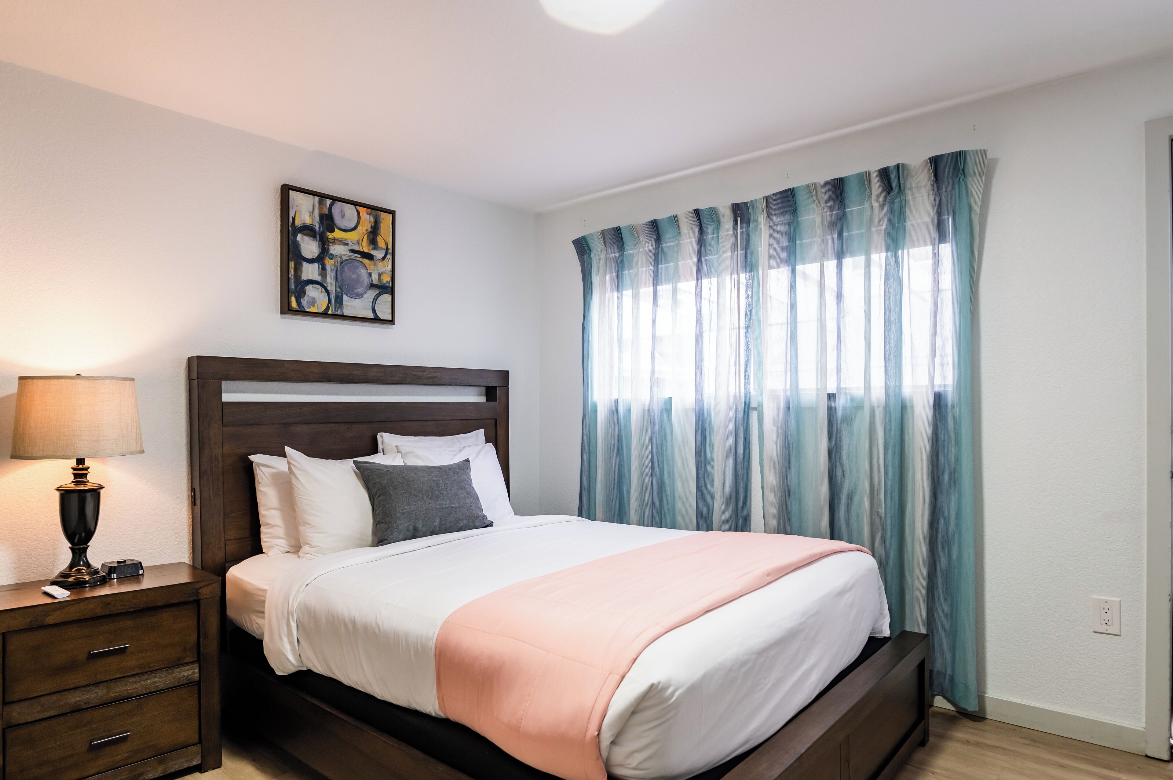 A neatly made bed with a wooden headboard, a bedside lamp, and a painting on the wall.