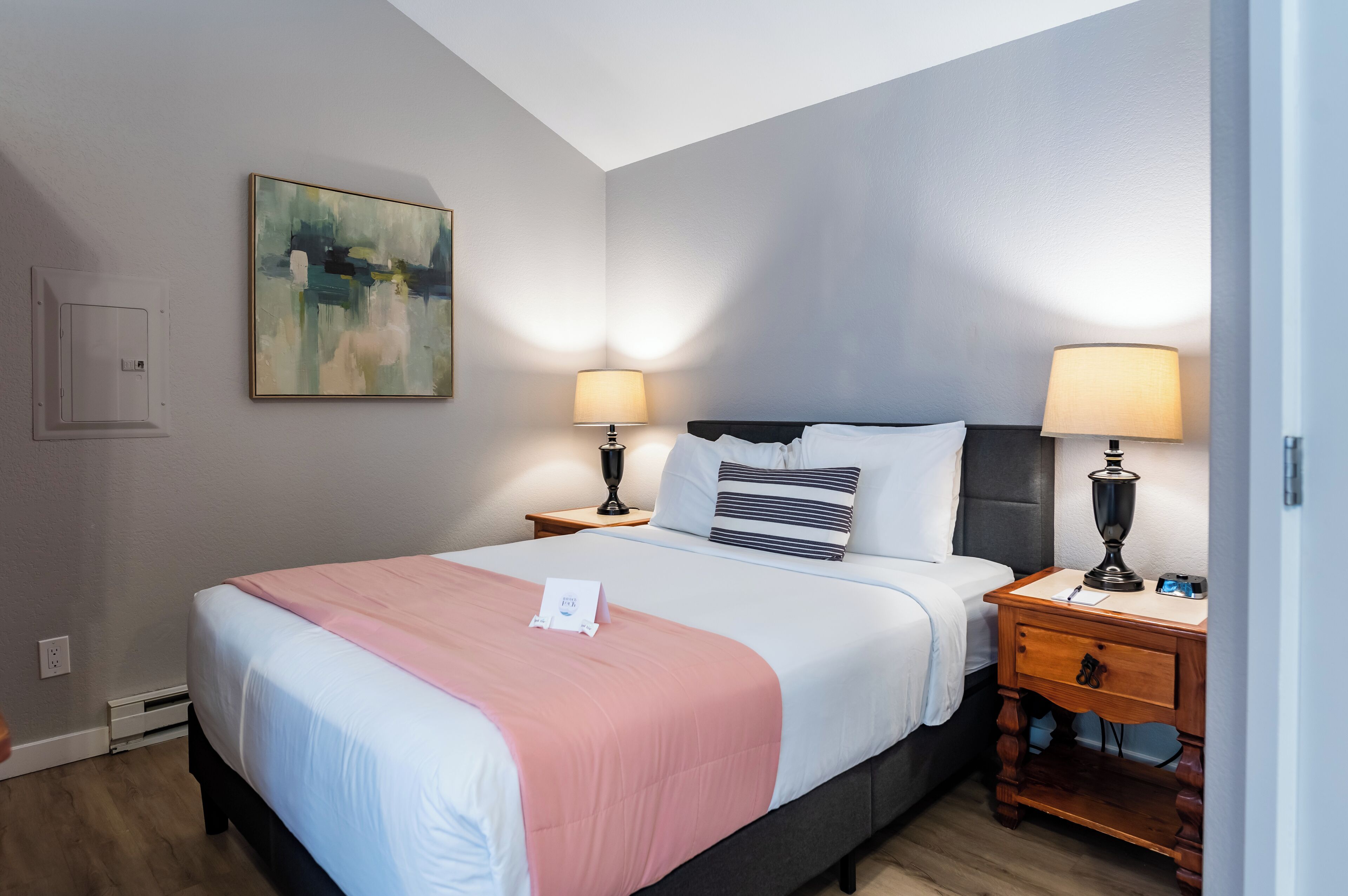 A hotel room with a bed, two bedside tables, a painting on the wall, and a night switch.