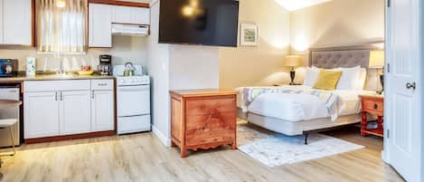 Una habitación de hotel pequeña con kitchenette, una cama con cabecera y un televisor montado en la pared.