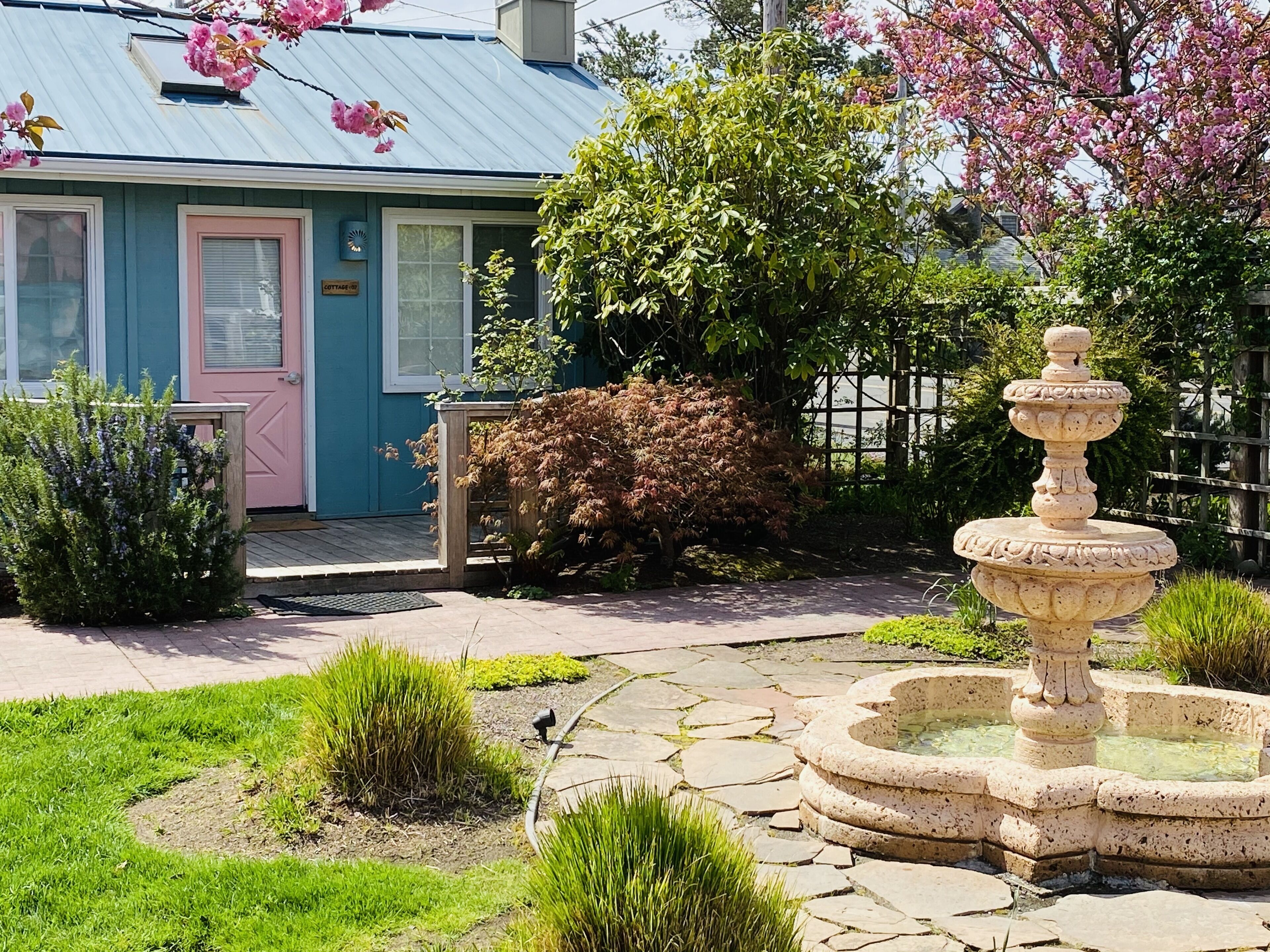 A cottage with a blue exterior, a pink door, and a stone fountain in the garden.