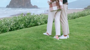 Una pareja se abraza en una zona verde con un promontorio rocoso y el océano al fondo.