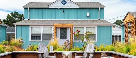 A two-story house with a front porch, a fire pit, and two Adirondack chairs.
