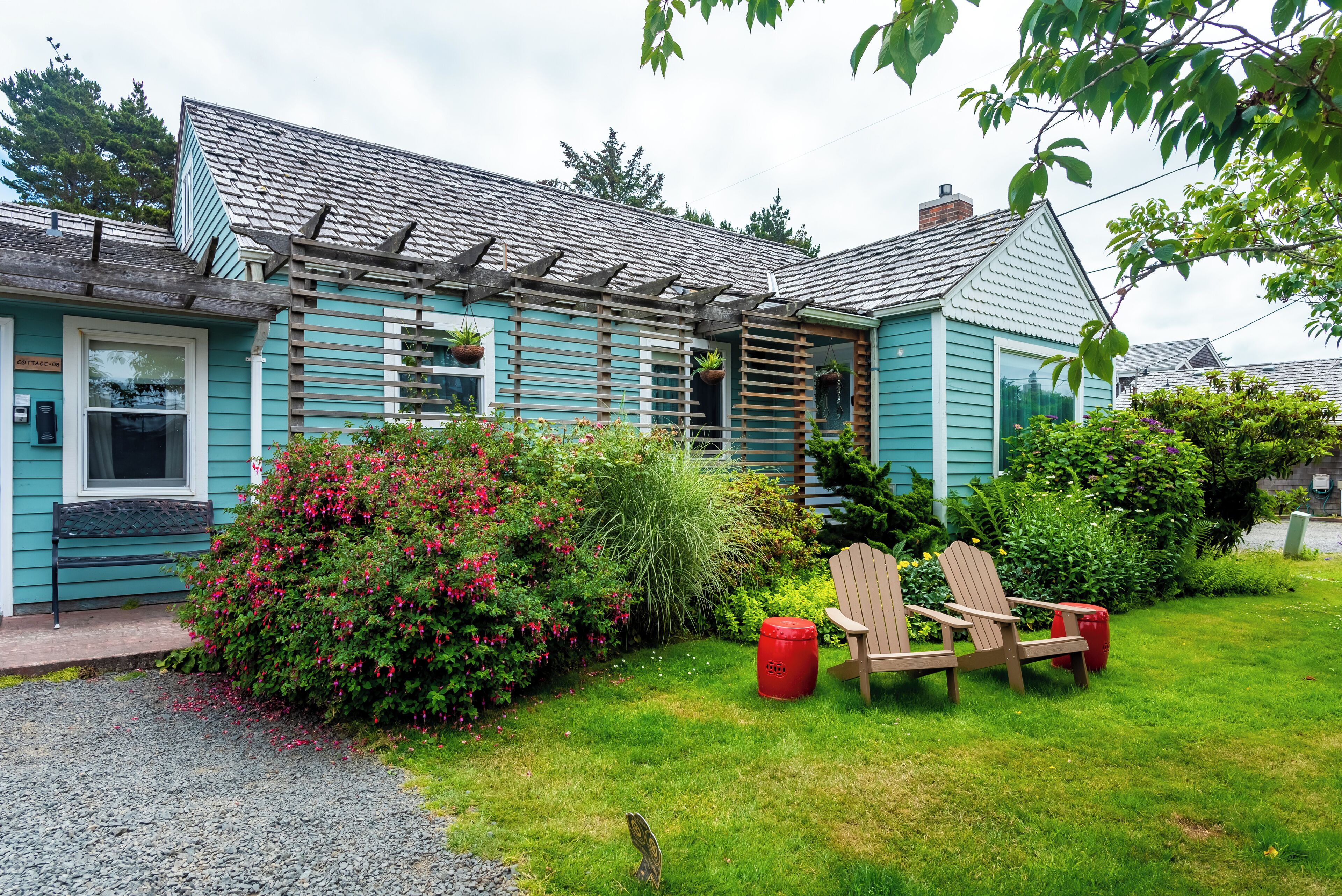 A house with a wooden deck, a garden with various plants, and a red trash can.