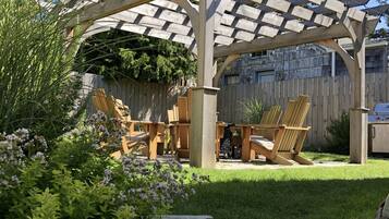 A wooden pergola with light fixtures, a barbecue grill, and outdoor seating with chairs and a table.