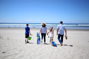 Uma família caminhando numa praia de areia, com o oceano ao fundo.