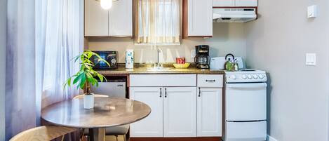 Una cocina compacta con comedor, estufa, cafetera y una planta en maceta.