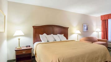 A hotel room with a large bed, two bedside tables with lamps, a red chair, and a window with red curtains.