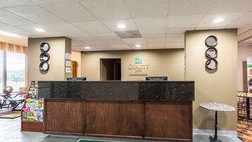 A hotel reception desk with a wooden counter, a sign above it, and a small table with a round tablecloth.