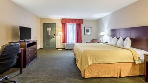 A hotel room with a bed, a desk with a television, a chair, a lamp, and a door. - Quality Inn Heber Springs (Heber Springs)