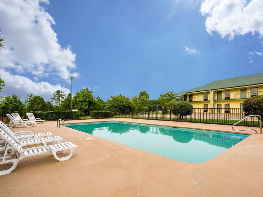 Une piscine avec des chaises longues, un ciel dégagé et un bâtiment en arrière-plan.