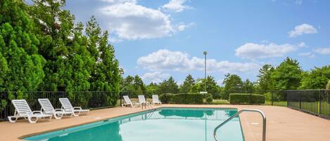 A swimming pool with a tiled deck, surrounded by a black fence, and white lounge chairs.