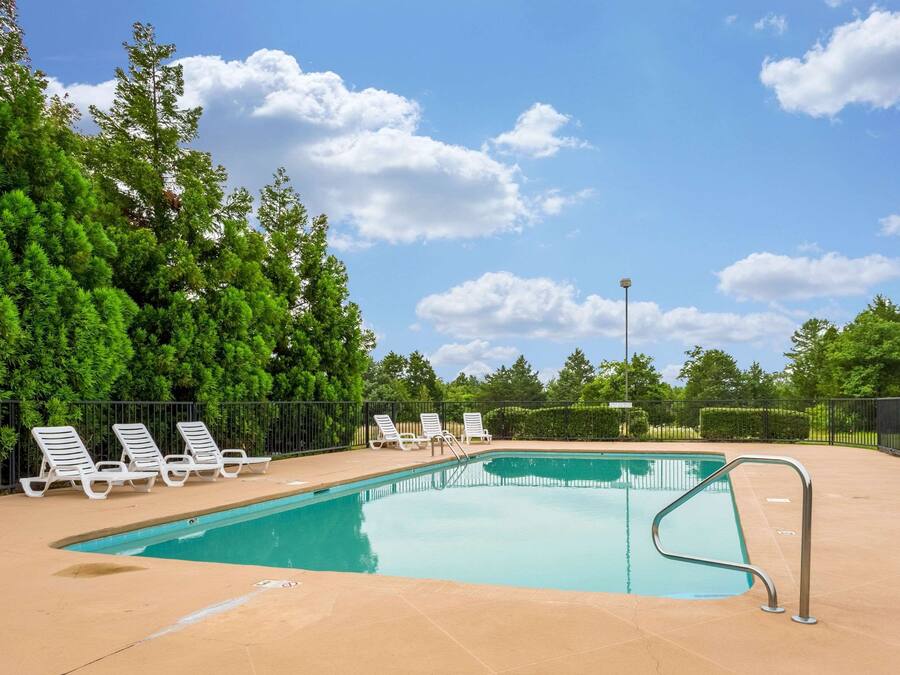 A swimming pool with a tiled deck, surrounded by a black fence, and white lounge chairs.