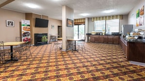 A hotel lobby with a patterned carpet, a fireplace, a television mounted on the wall, and a kitchen area with a buffet. - Quality Inn Heber Springs (Heber Springs)