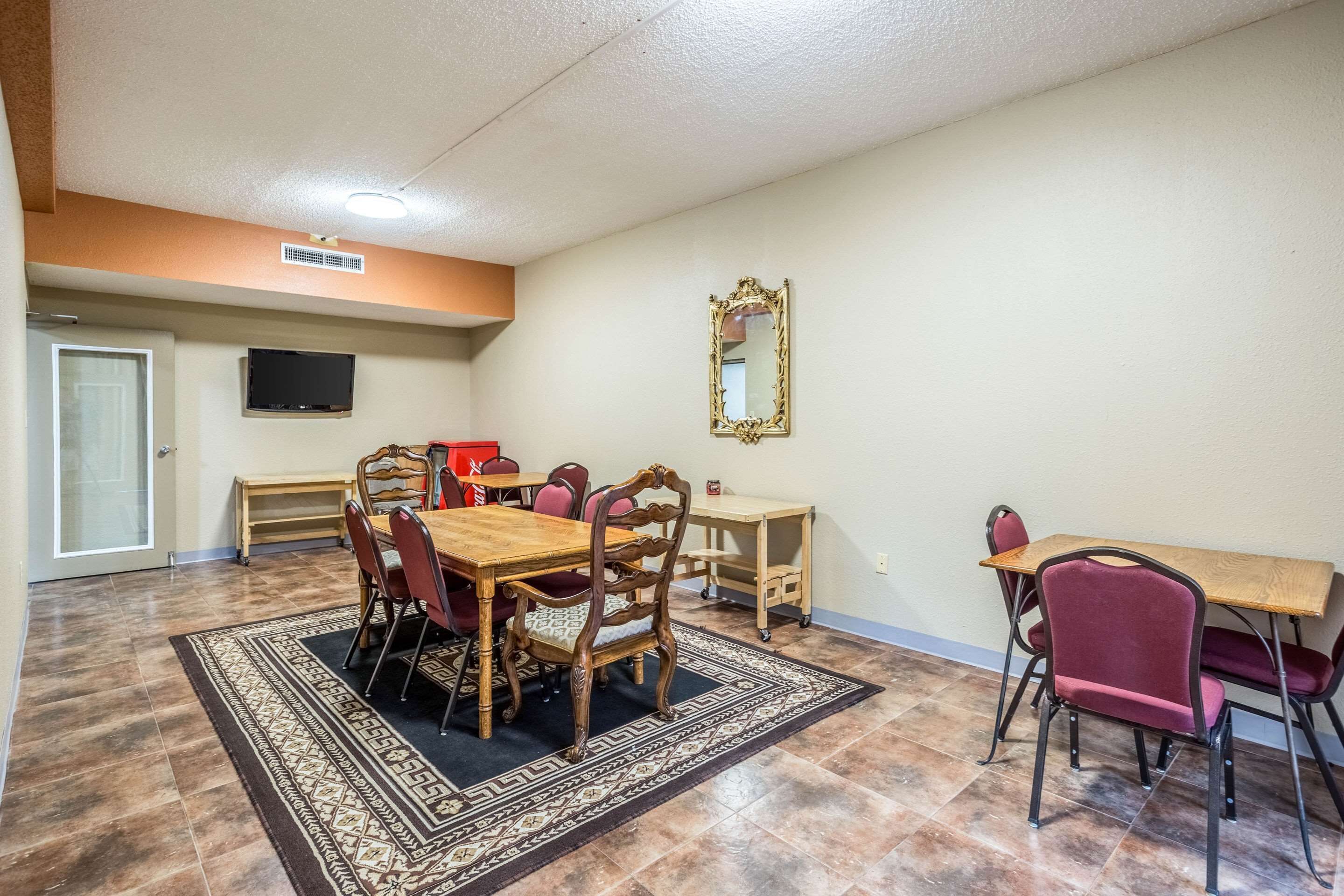 A dining area with a wooden table and chairs, a patterned rug, a television on the wall, and a mirror.