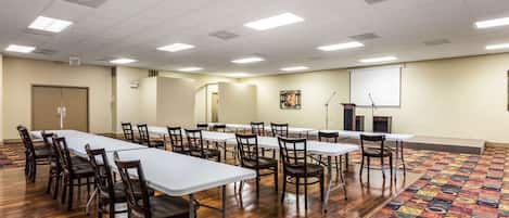 A conference room with long tables, chairs, a projector screen, and a carpeted floor.