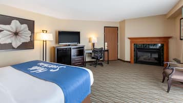 Quarto de hotel com cama, escrivaninha, cadeira, televisão, luminárias e lareira.