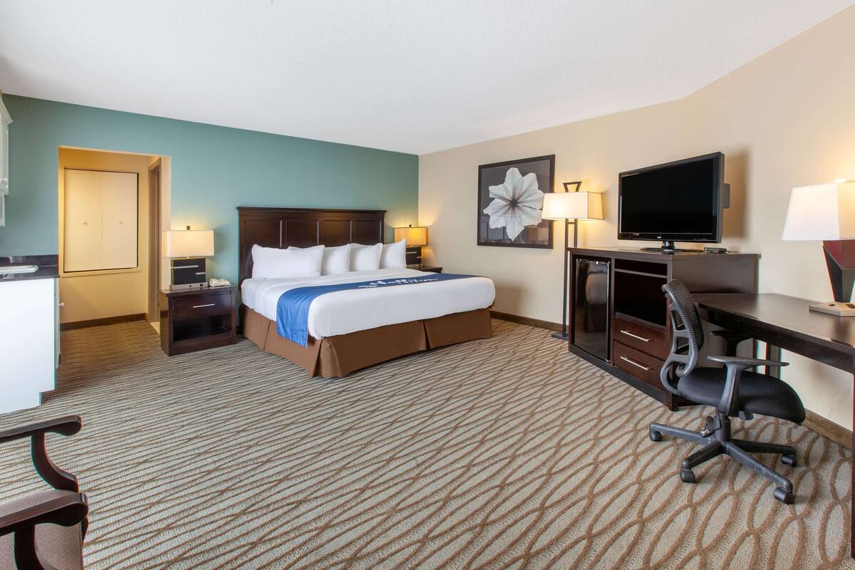 A hotel room with a large bed, a desk with a computer, a television, and two bedside lamps.