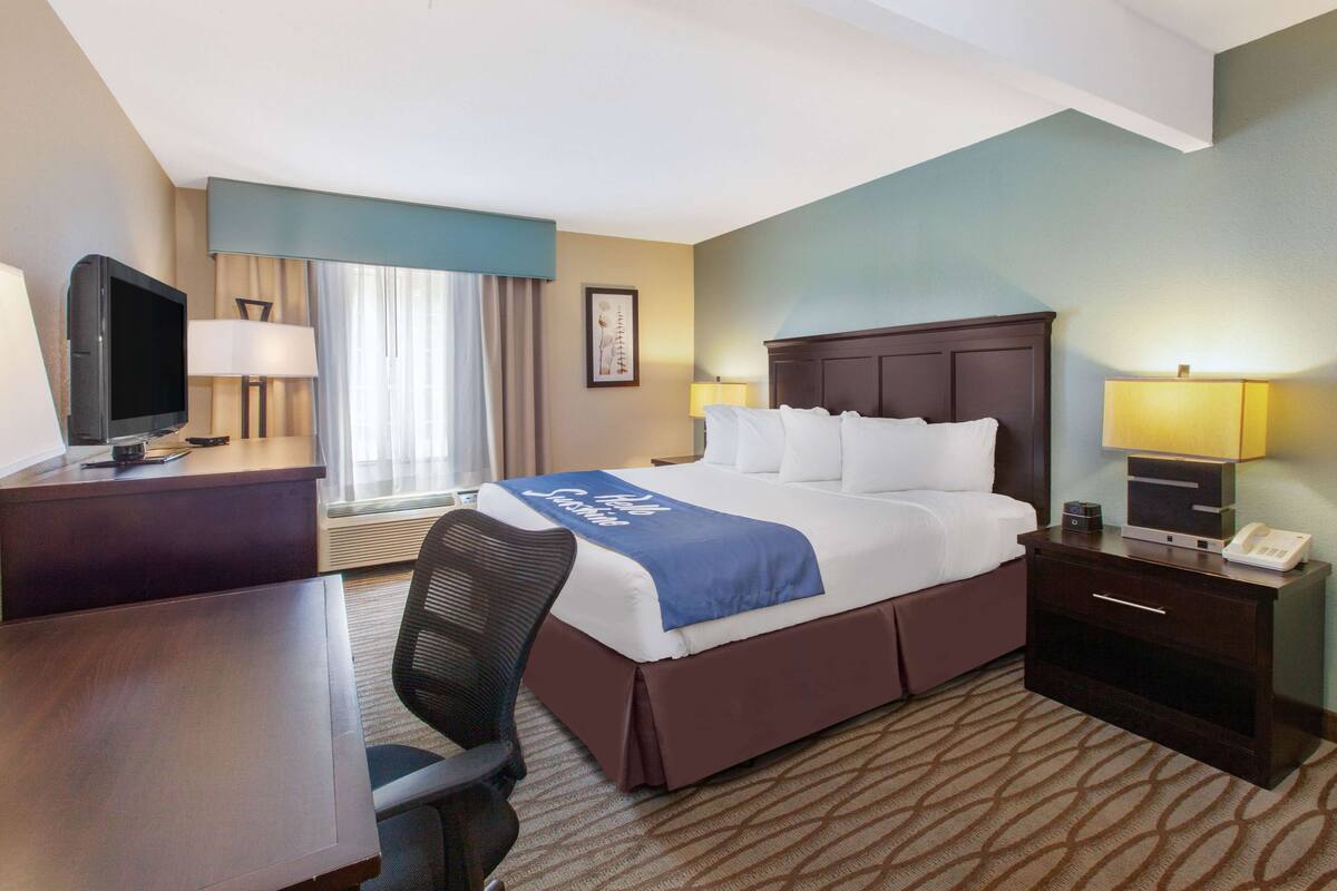 A hotel room with a bed, desk, chair, and a television.