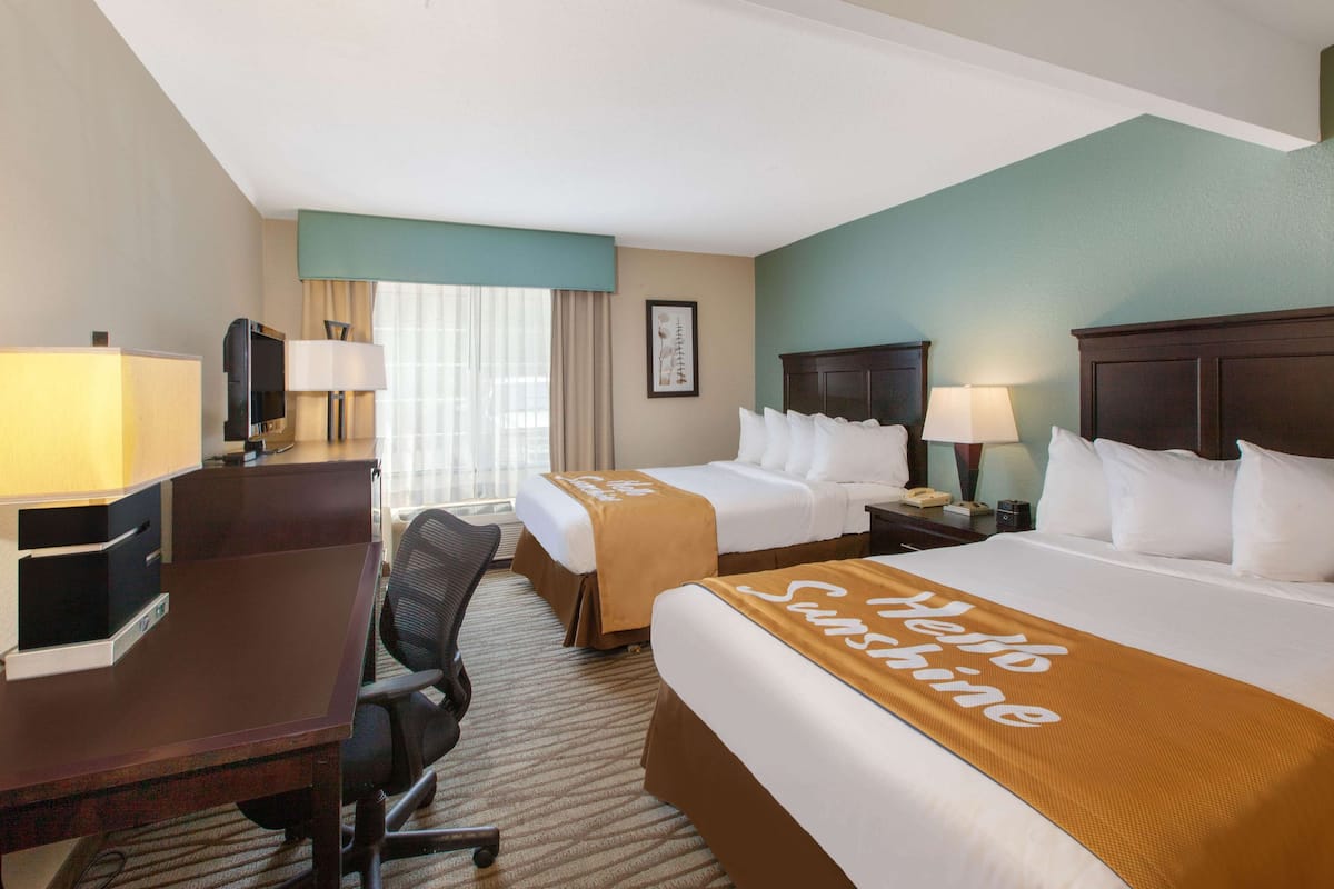 A hotel room with two beds, a desk, a chair, a TV, and a window with curtains.