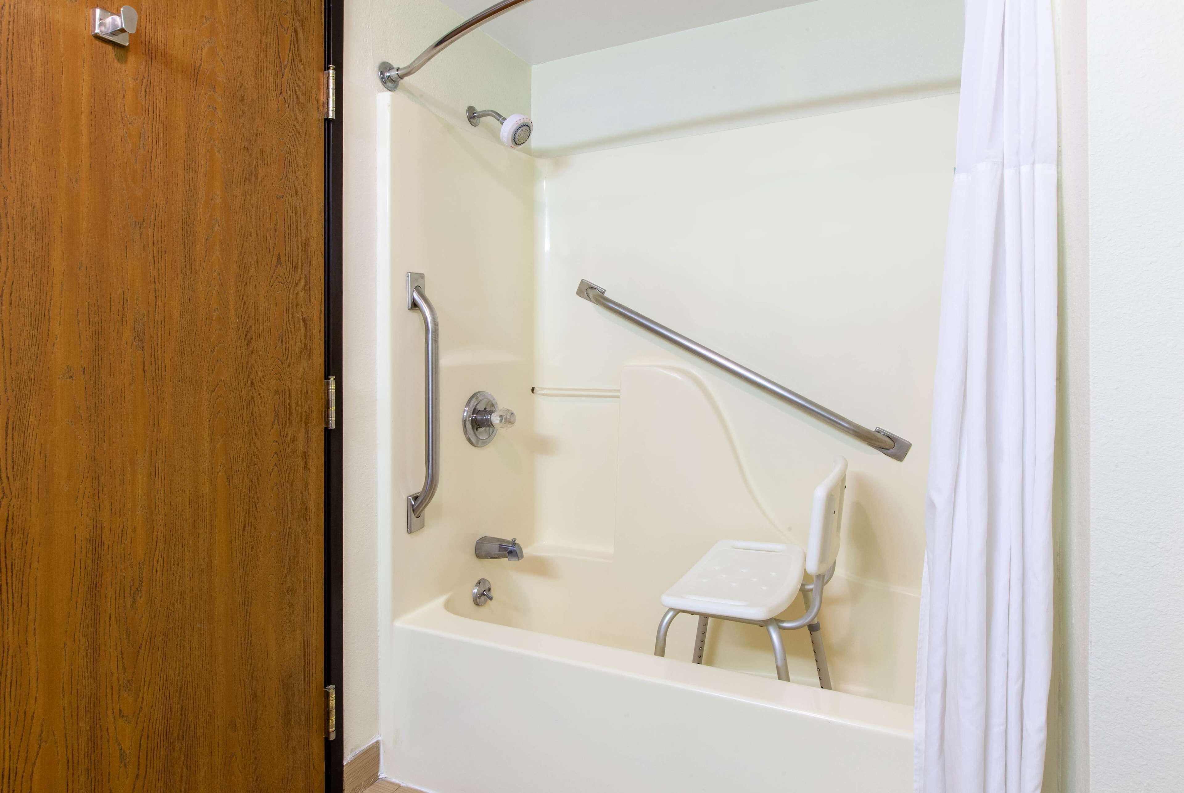 Een badkamer met een bad, een douche en een witte stoel.