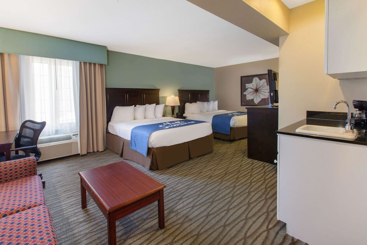 A hotel room with a bed, a desk, a chair, a small table, and a kitchenette.