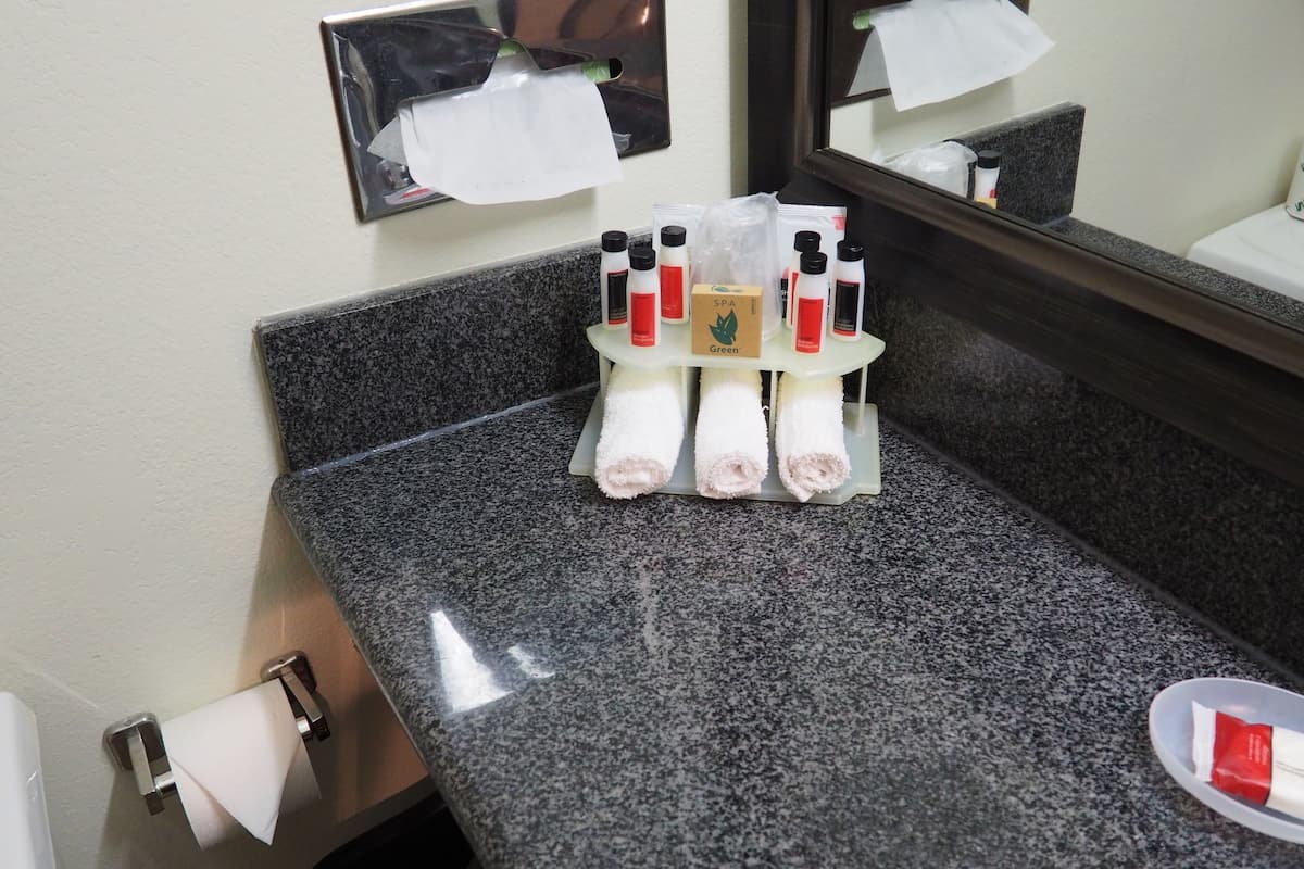 A bathroom with a granite countertop, a mirror, and toiletries including bottles and a box labeled "SPA Green".