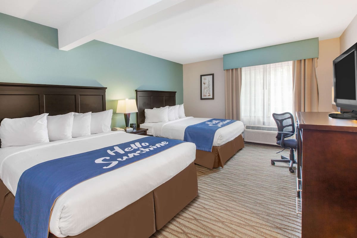 A hotel room with two beds, a desk, a chair, a television, and a window with curtains.