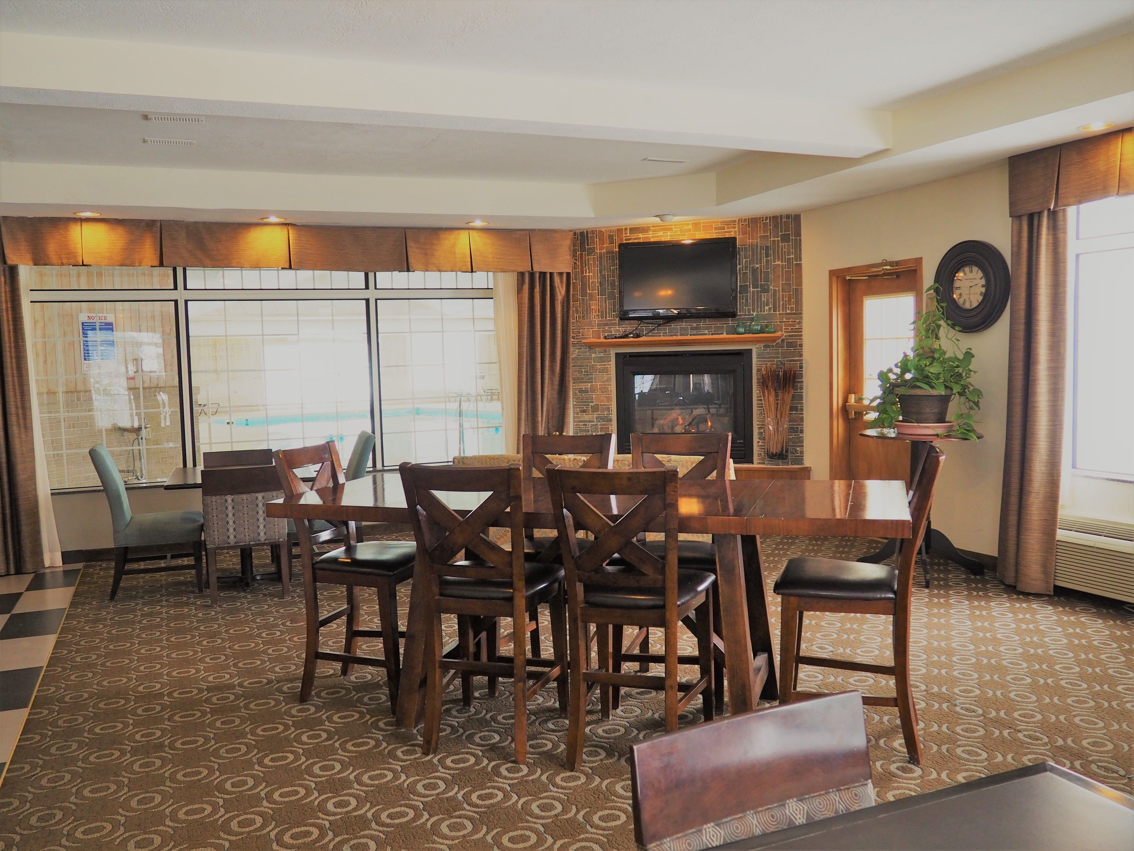 A dining area with a fireplace, a television mounted above it, and a large window with a view of a pool.