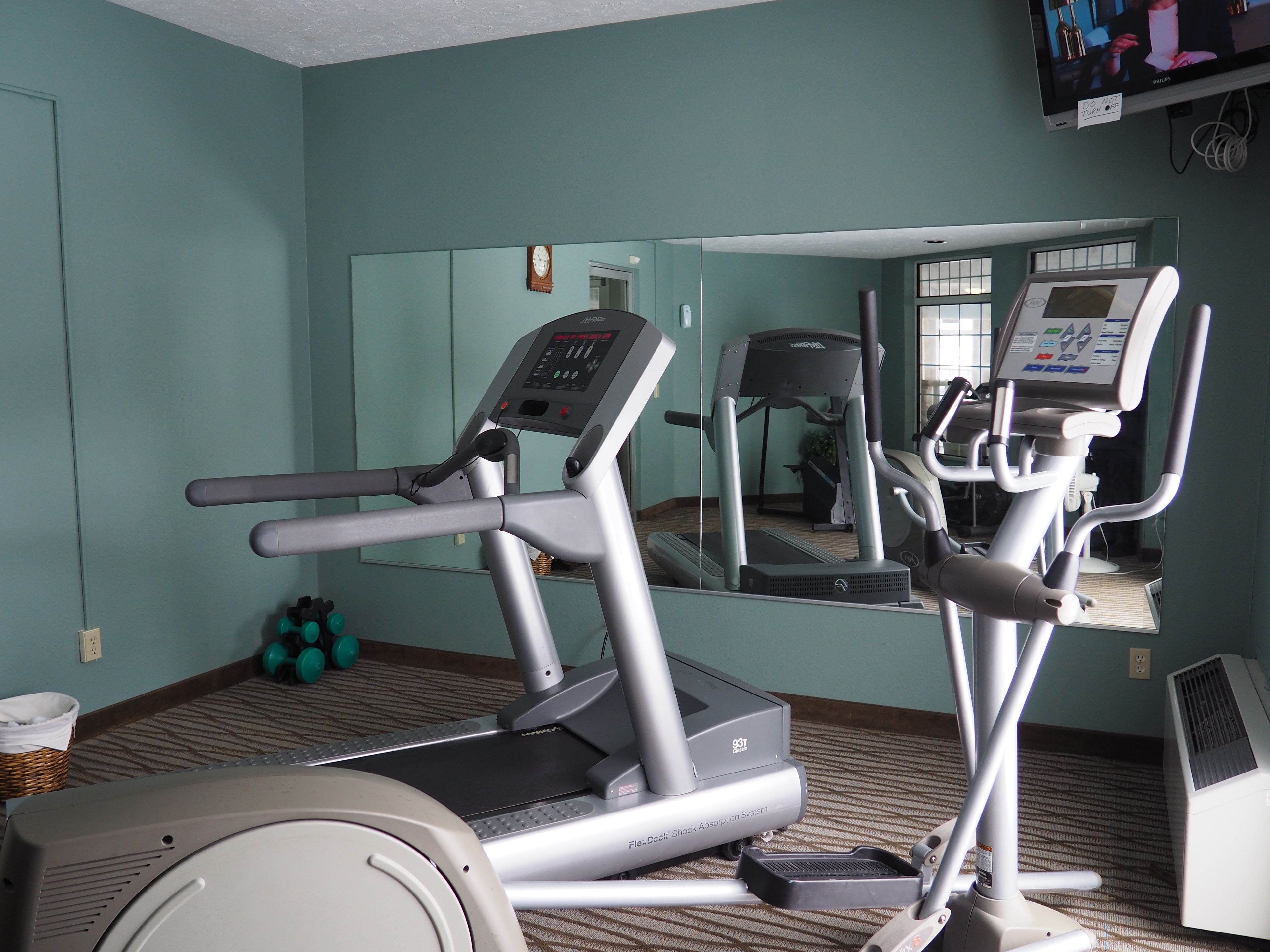 Un gimnasio con cintas de correr y un espejo grande.