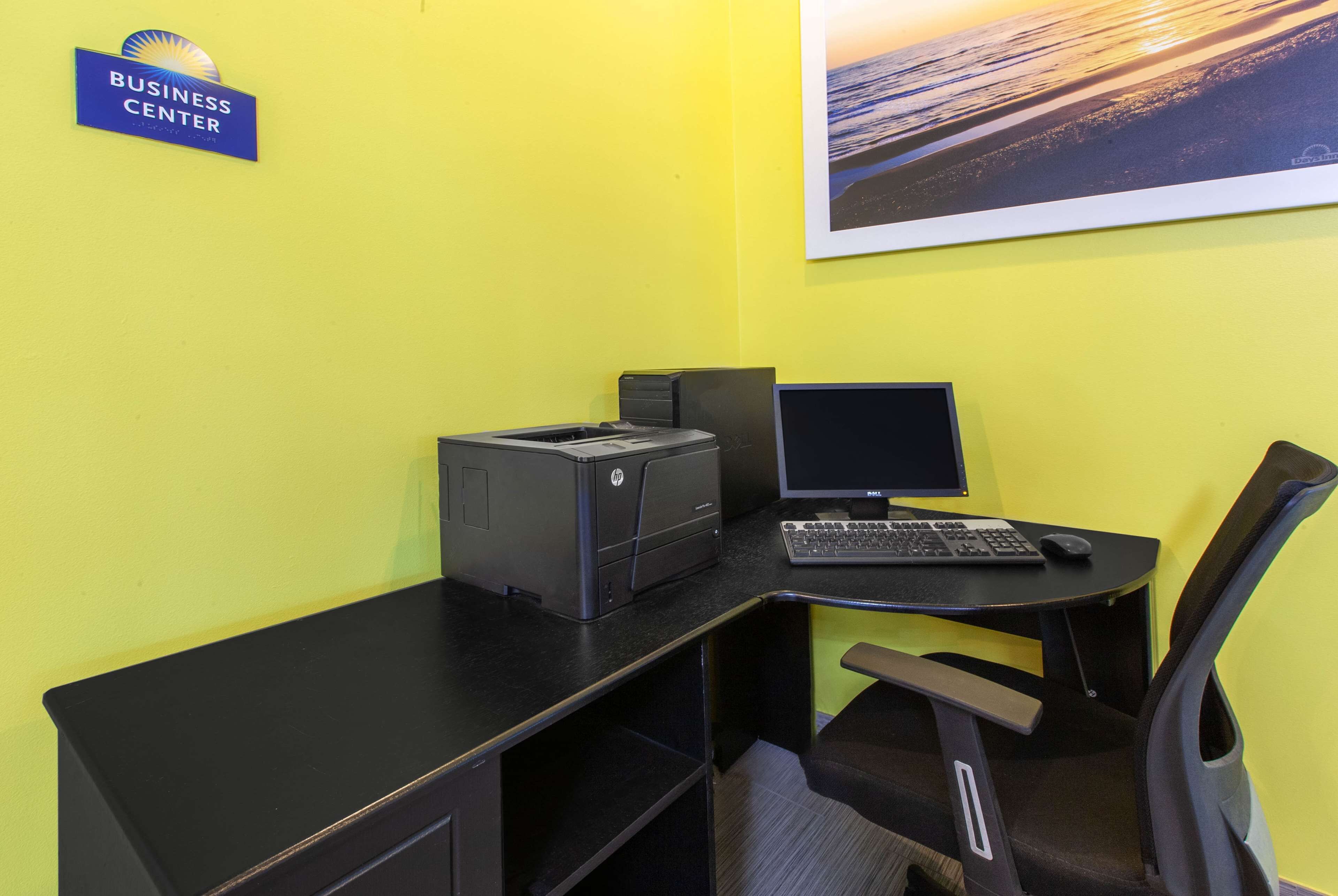 A business center desk with a printer, monitor, and keyboard, a chair, and a sign indicating the business center location.