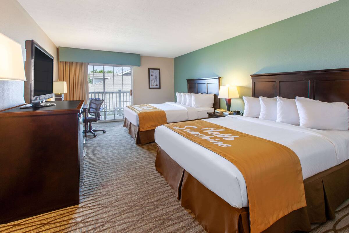 A hotel room with two beds, a desk, a chair, a TV, and a balcony.