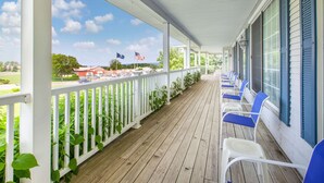 A covered porch with white railings, blue chairs, and a view of a road with flags. - Days Inn by Wyndham Petoskey (Petoskey)
