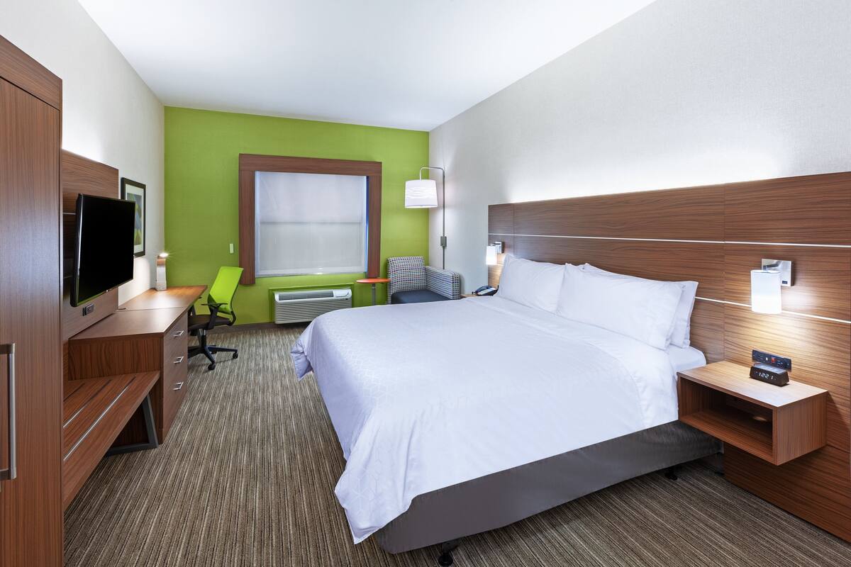 A hotel room with a large bed, a desk with a chair, a television, and a window with blinds.