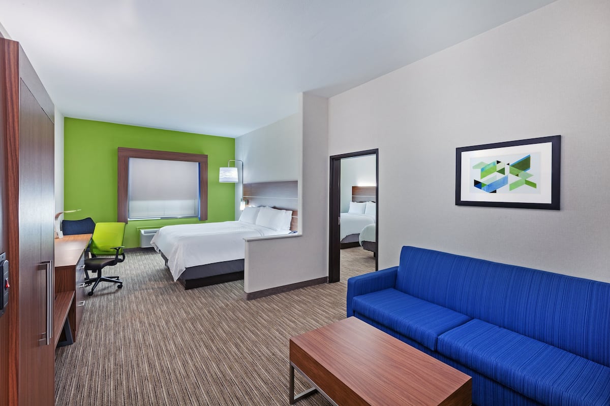 A hotel room with a bed, a blue sofa, a desk, a chair, and a framed picture on the wall.