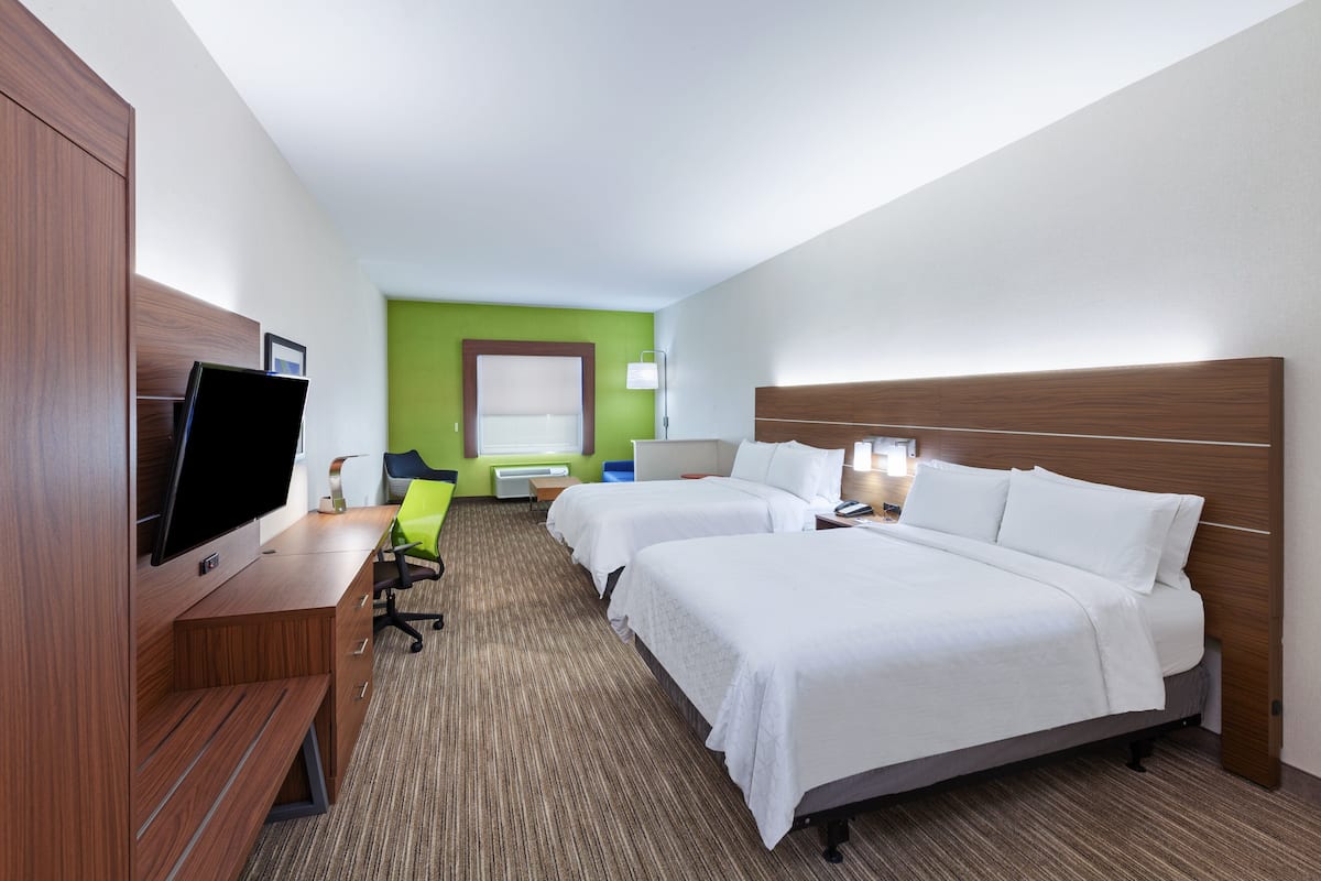 A hotel room with two beds, a desk with a flat-screen TV, a chair, and a green accent wall.