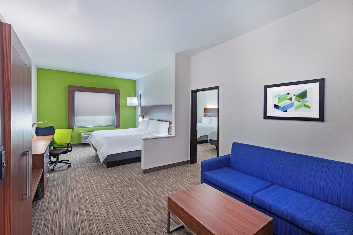 Une chambre d’hôtel avec un lit, un canapé bleu, un bureau, une chaise et un tableau encadré au mur.