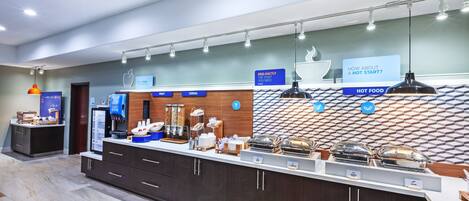 A modern breakfast bar with labeled food stations, including fruit and cereal, and a sign offering a hot start.