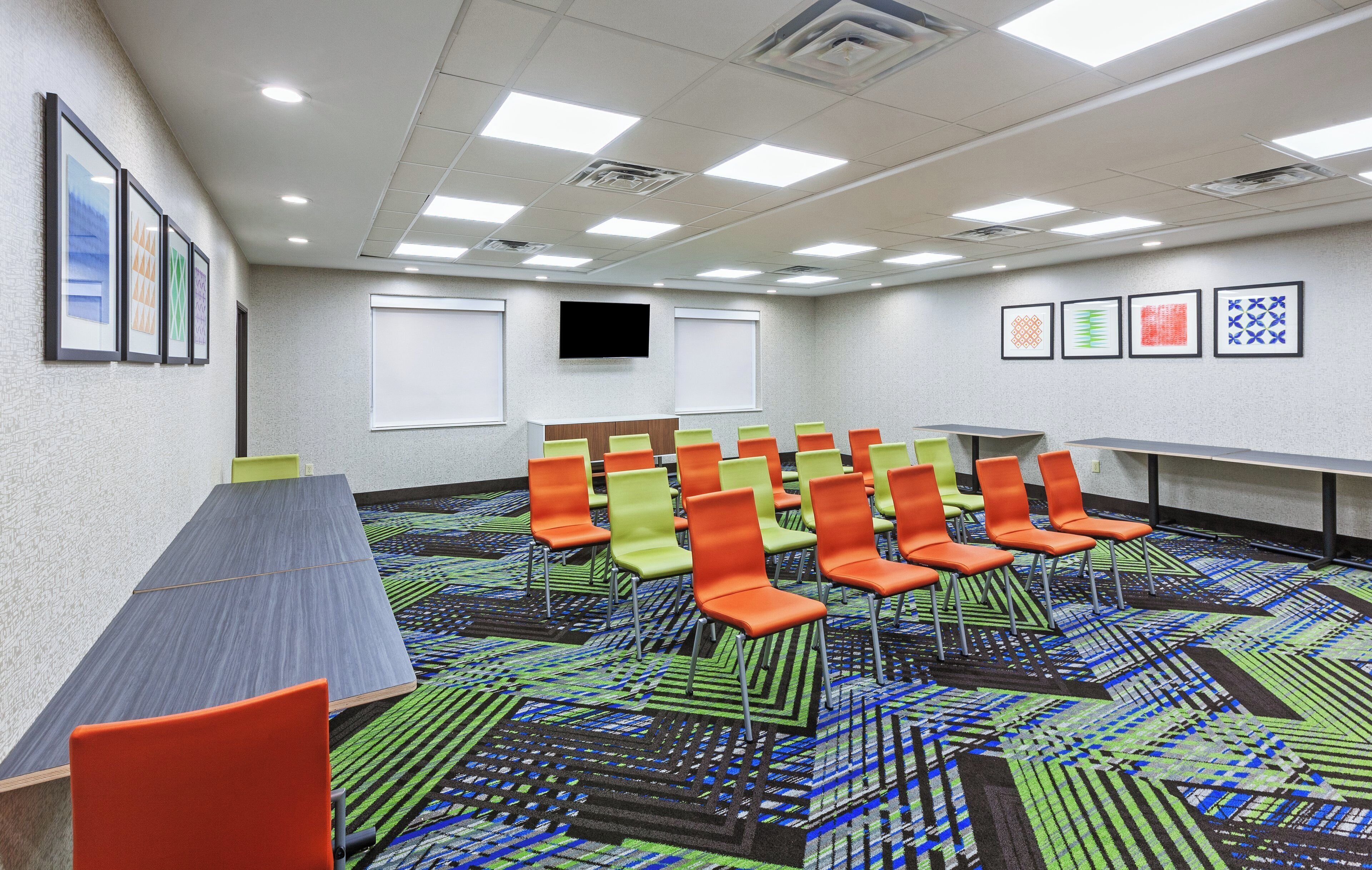 Uma sala de conferências com uma mesa comprida, várias cadeiras, uma tela de projetor e uma televisão.