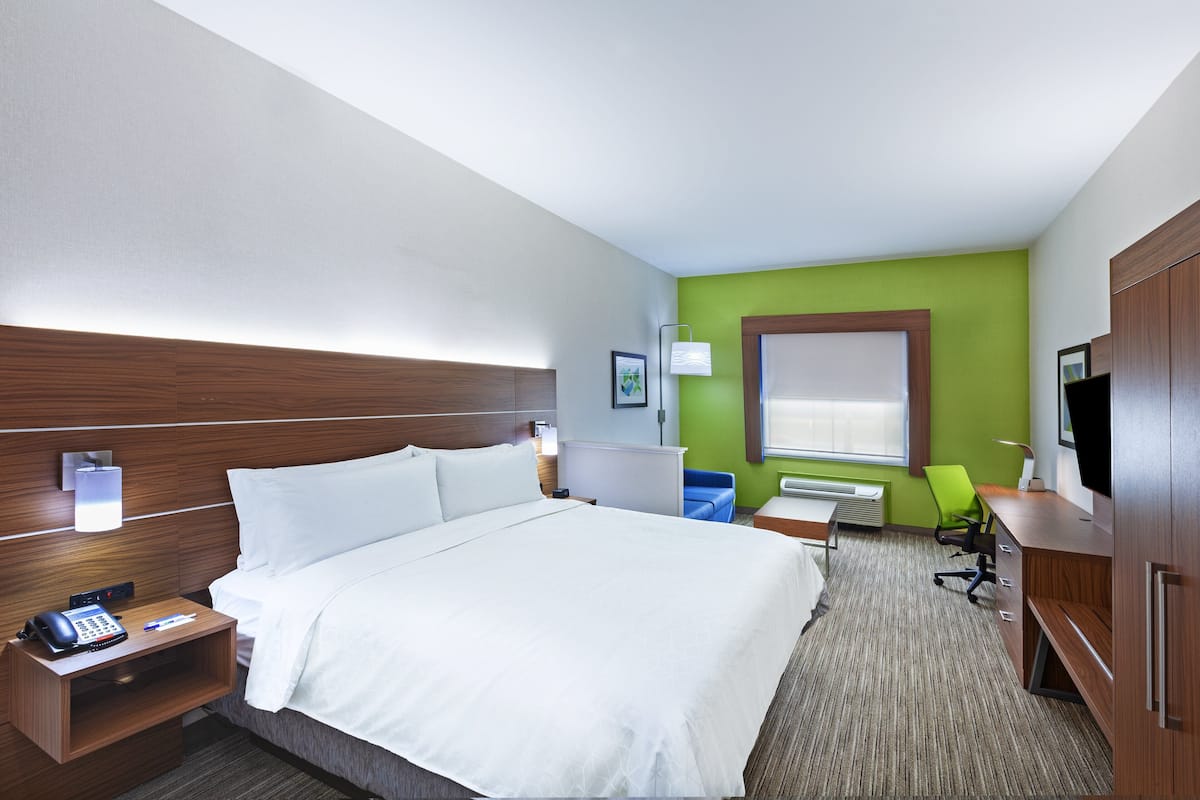 A hotel room with a large bed, bedside tables, a desk, a chair, and a television.