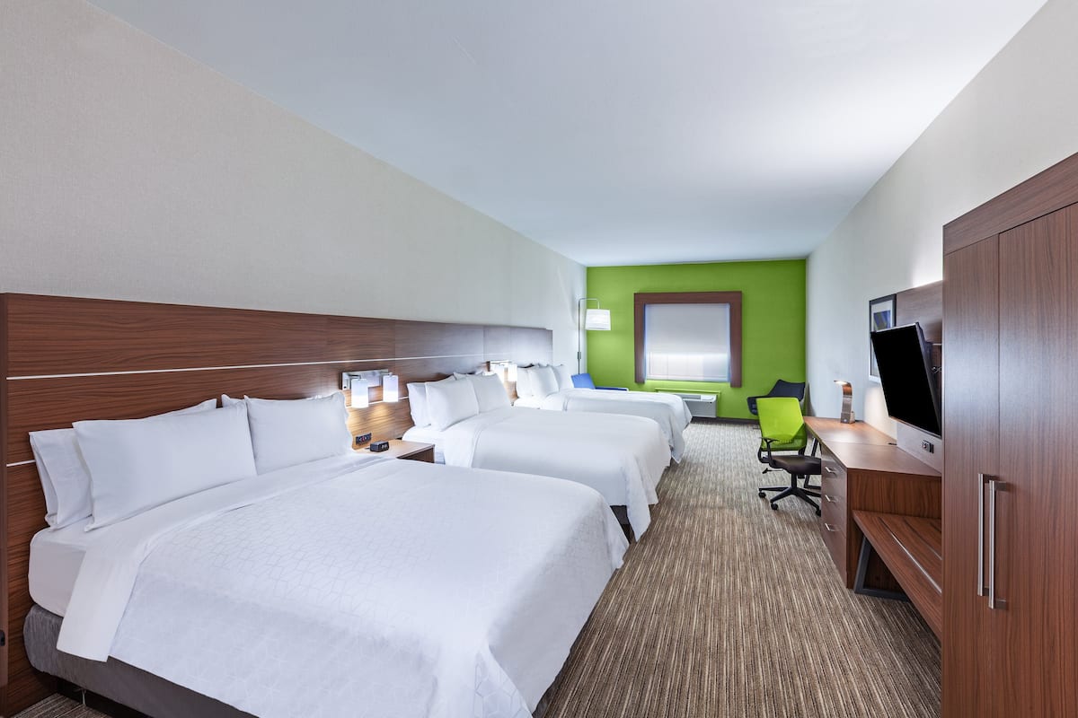 A hotel room with three beds, a desk with a computer, and a television.